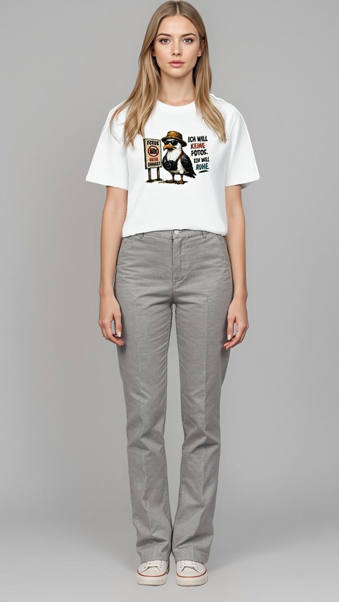 Frau in grauer Hose und weißem Oversized-Shirt mit Möwen-Motiv, Ganzkörperaufnahme vor grauem Hintergrund.