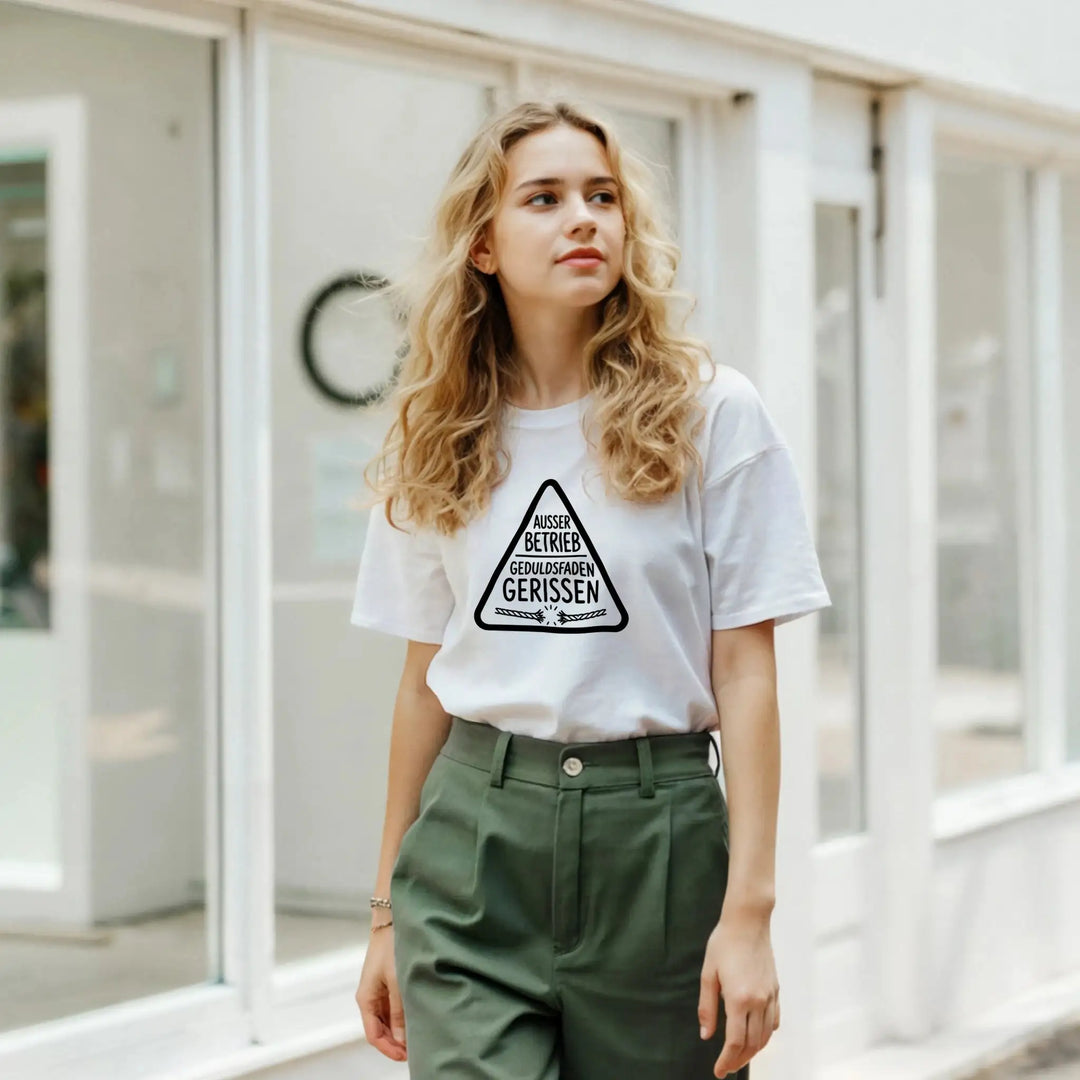 Junge Frau in grüner Hose trägt weißes „Geduldsfaden gerissen“ T-Shirt vor Schaufenster
