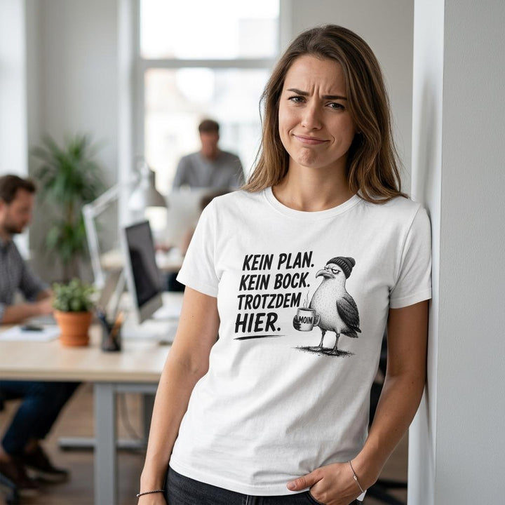 Frau lehnt im Büro an einer Wand, weißes T-Shirt mit Spruch „Kein Plan. Kein Bock. Trotzdem hier.“
