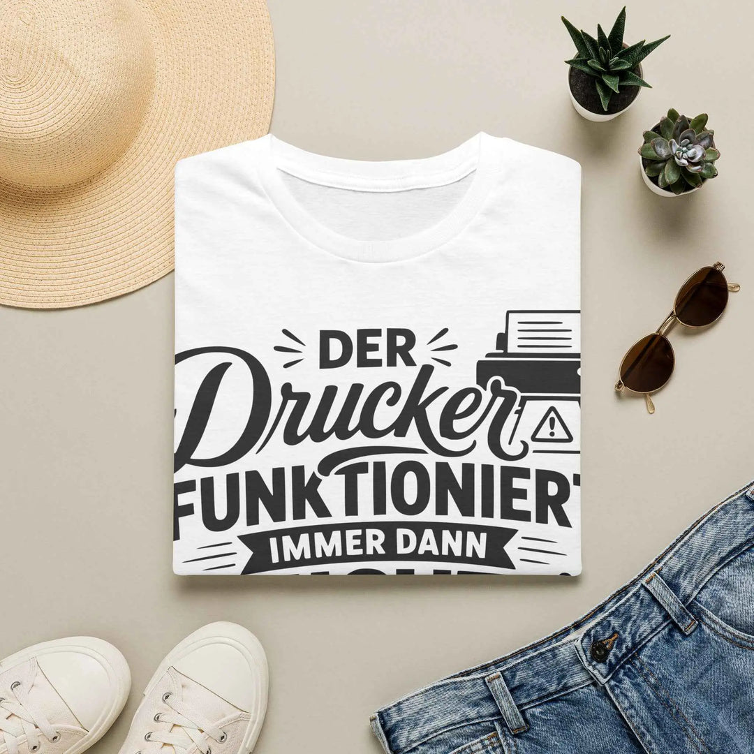 Weißes T-Shirt mit dem Aufdruck „Der Drucker funktioniert immer dann nicht, wenn du es am wenigsten brauchst. Also: immer.“ als Flatlay zwischen Sonnenhut, Sonnenbrille, Turnschuhen und Jeans.