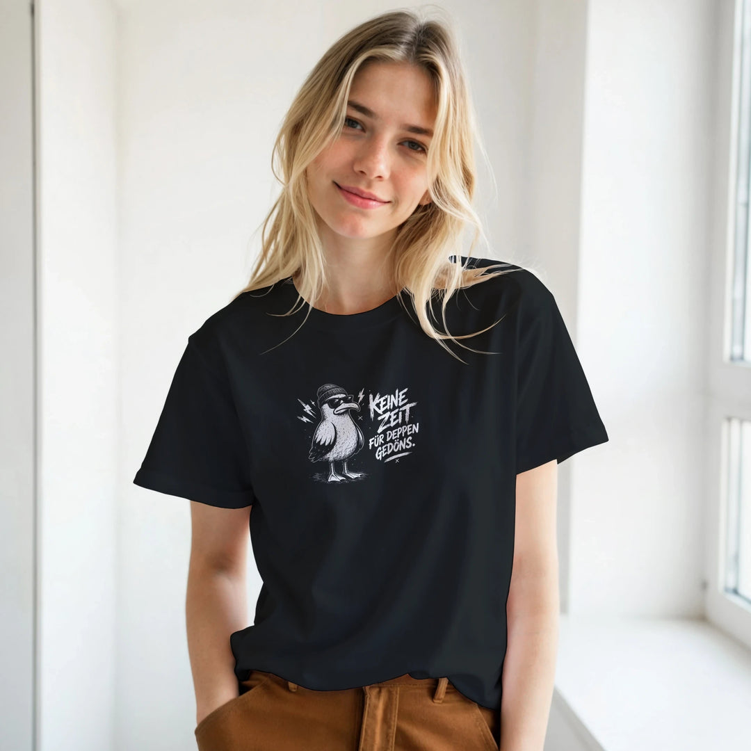 Blonde Frau lächelt am Fenster im schwarzen T-Shirt mit Möwen-Motiv und Schriftzug „Keine Zeit für Deppen-Gedöns.“