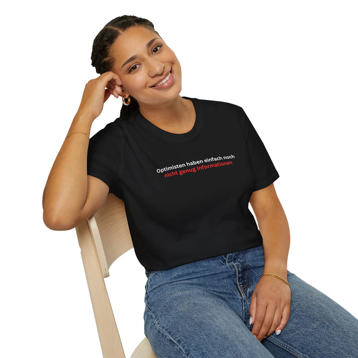 Lächelnde Frau auf Stuhl trägt schwarzes „Optimisten“-T-Shirt