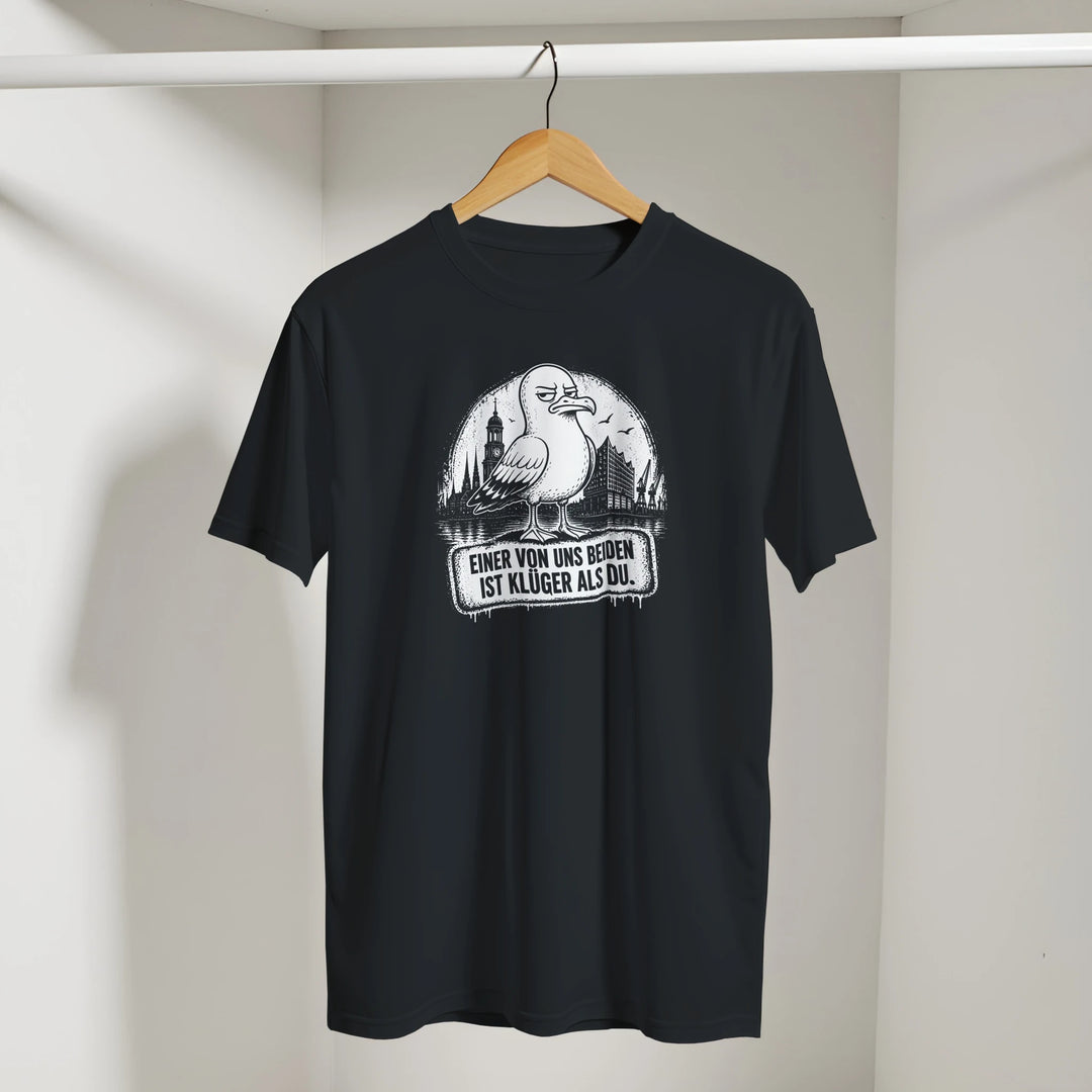 Schwarzes T-Shirt mit Möwe und Hamburg-Skyline an einem Holzbügel hängend in einer Umkleide.