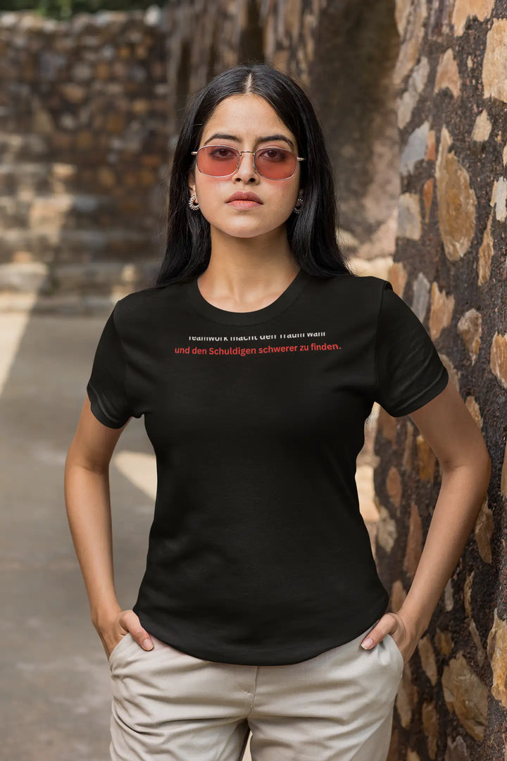 Frau mit Sonnenbrille vor Steinmauer trägt schwarzes „Teamwork“-T-Shirt
