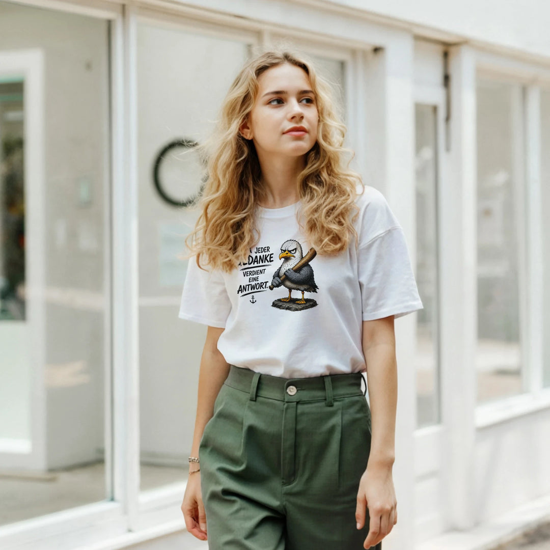 Frau mit grüner Hose trägt weißes T-Shirt mit Möwen-Print vor einem Schaufenster.