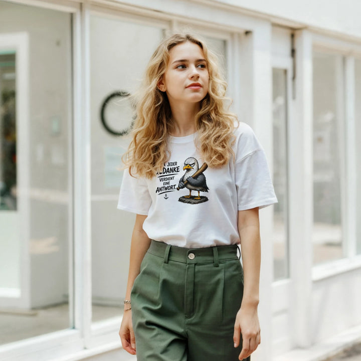 Frau mit grüner Hose trägt weißes T-Shirt mit Möwen-Print vor einem Schaufenster.