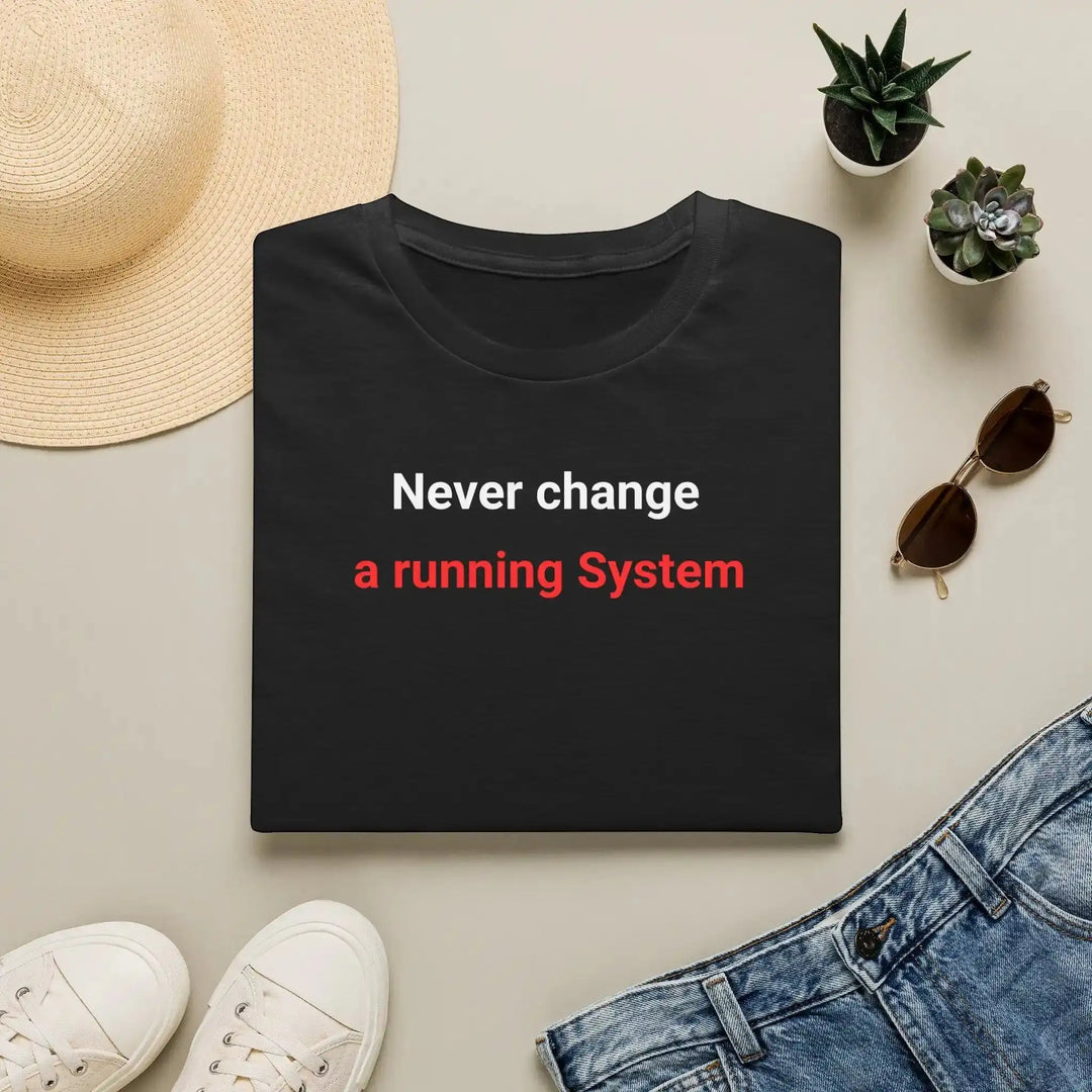 Schwarzes „Never change a running System“-T-Shirt als Flatlay zwischen Sonnenhut, Sonnenbrille, Turnschuhen und Jeans.