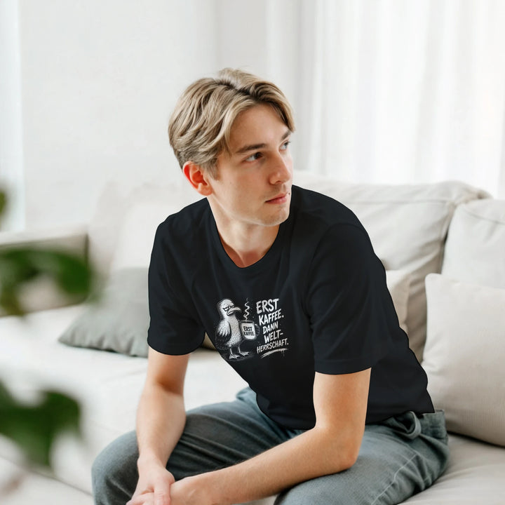 Junger Mann sitzt entspannt auf einem Sofa, trägt schwarzes T-Shirt mit Kaffee-Möwe
