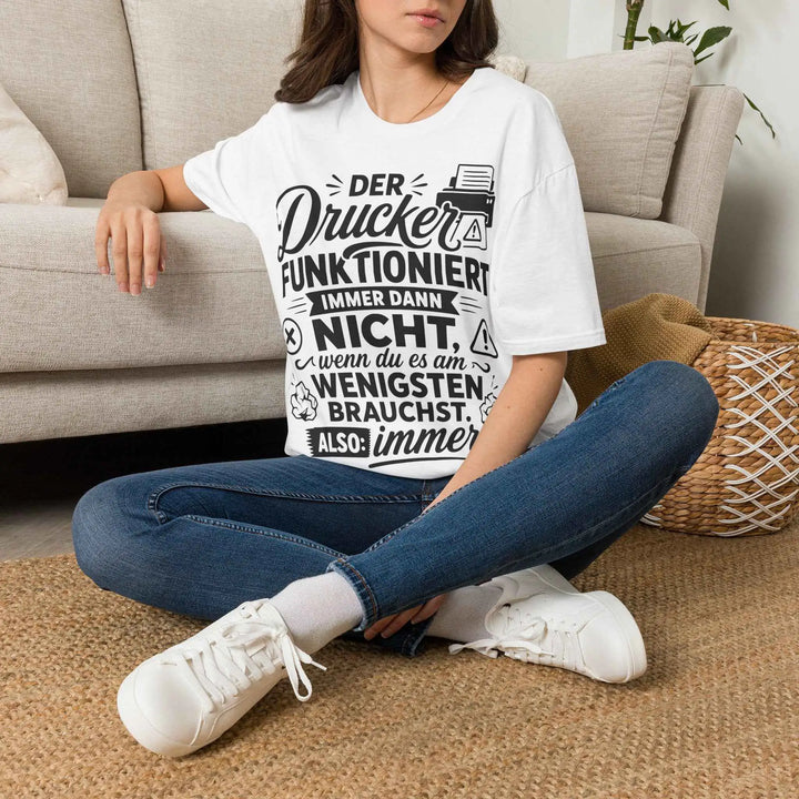 Frau sitzt locker auf dem Boden vor einem Sofa und trägt das weiße Drucker-Statement-Shirt mit Jeans und Sneakers.