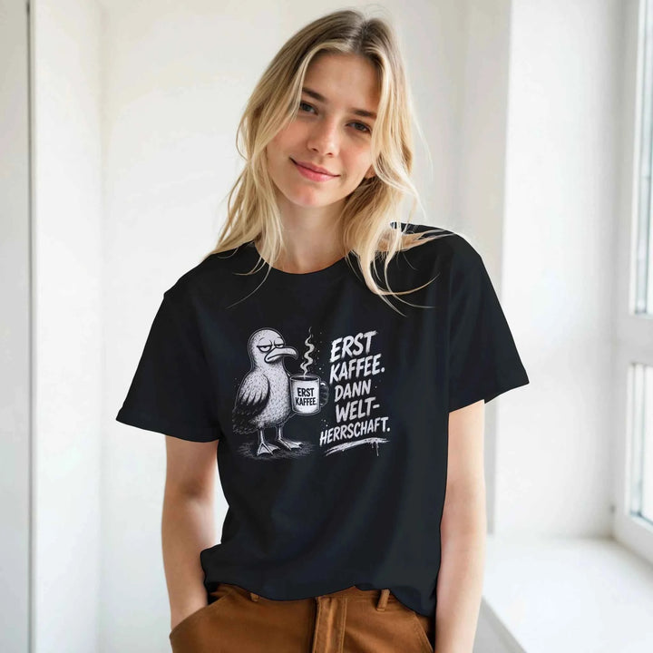 Junge Frau in schwarzem T-Shirt mit Kaffee-Möwen-Print, lächelnd am Fenster stehend