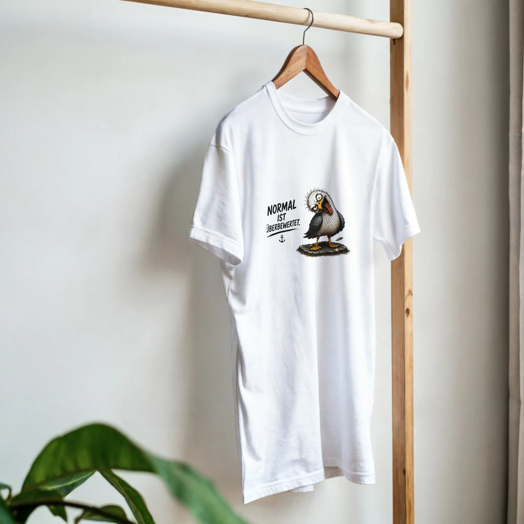 Weißes T-Shirt mit Möwen-Print hängt an einem Holzkleiderständer neben einer Zimmerpflanze