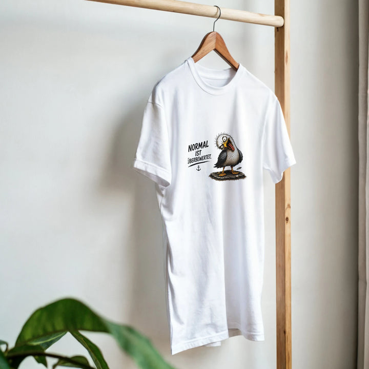 Weißes T-Shirt mit Möwen-Print hängt an einem Holzkleiderständer neben einer Zimmerpflanze