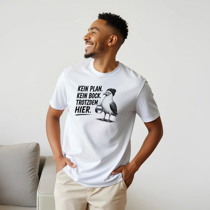 Lächelnder Mann im Wohnzimmer mit Händen in den Taschen, weißes T-Shirt mit Möwen-Motiv