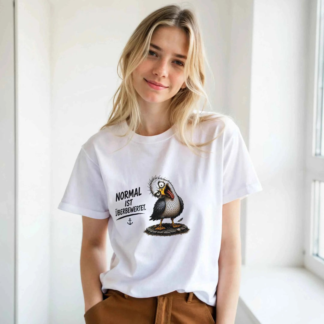 Blonde Frau trägt weißes T-Shirt mit Möwen-Print, lächelnd am hellen Fenster stehend