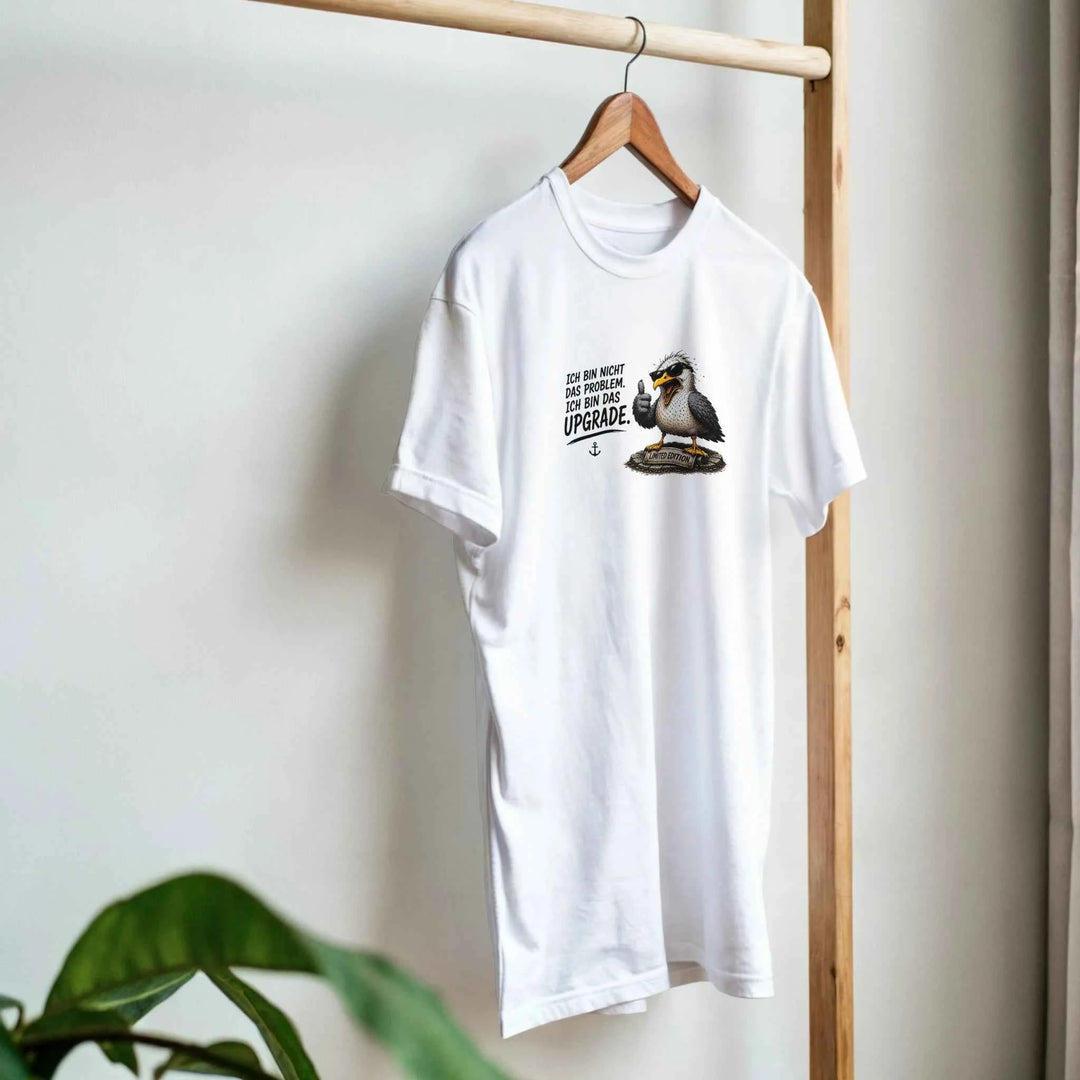 Weißes T-Shirt mit Möwen-Motiv hängt an einem Holzkleiderständer neben einer Zimmerpflanze