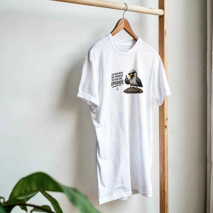 Weißes T-Shirt mit Möwen-Motiv hängt an einem Holzkleiderständer neben einer Zimmerpflanze