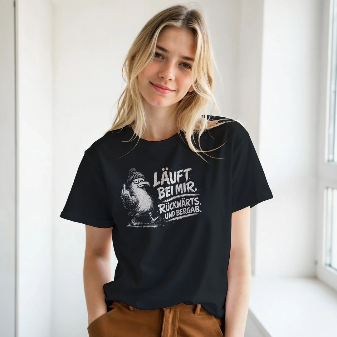 Frau trägt das schwarze T-Shirt mit Möwen-Print vor heller Fensterwand, kombiniert mit brauner Hose.