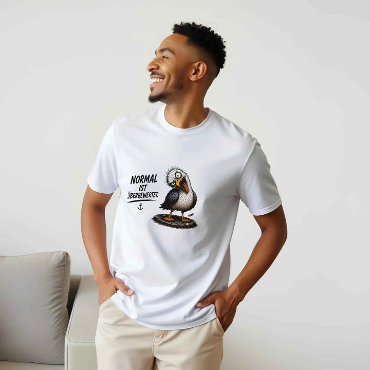 Lachender Mann in weißem T-Shirt mit Möwen-Motiv, sitzend auf einem hellen Sofa