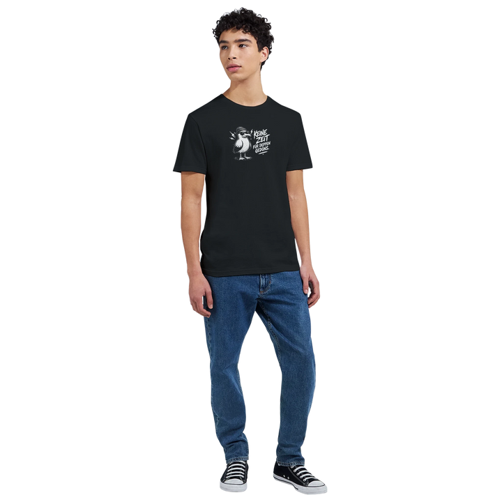 Ganzkörperaufnahme eines Mannes in Jeans und Sneakers, schwarzes T-Shirt mit Möwen-Print auf der Brust vor hellem Hintergrund.