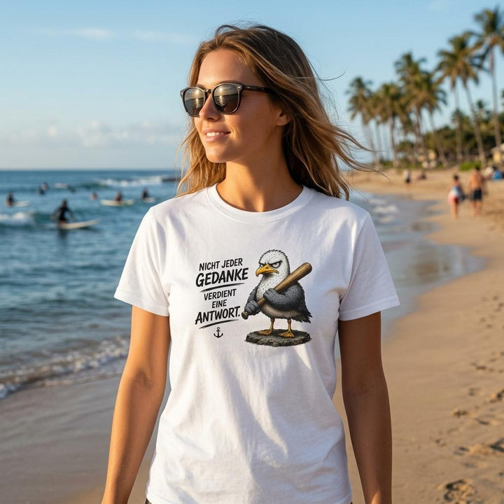 Frau am Strand trägt weißes T-Shirt mit Möwe und Baseballschläger, im Hintergrund Surfer und Palmen.