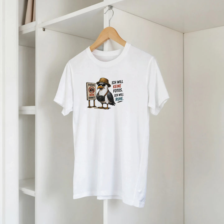 Weißes T-Shirt mit Möwen- und Kamera-Motiv hängt auf einem Holzbügel im Kleiderschrank.