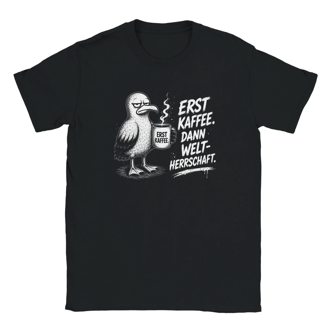 Flatlay des schwarzen T-Shirts mit Möwen-Motiv und Spruch „Erst Kaffee. Dann Weltherrschaft.“ auf grauem Hintergrund