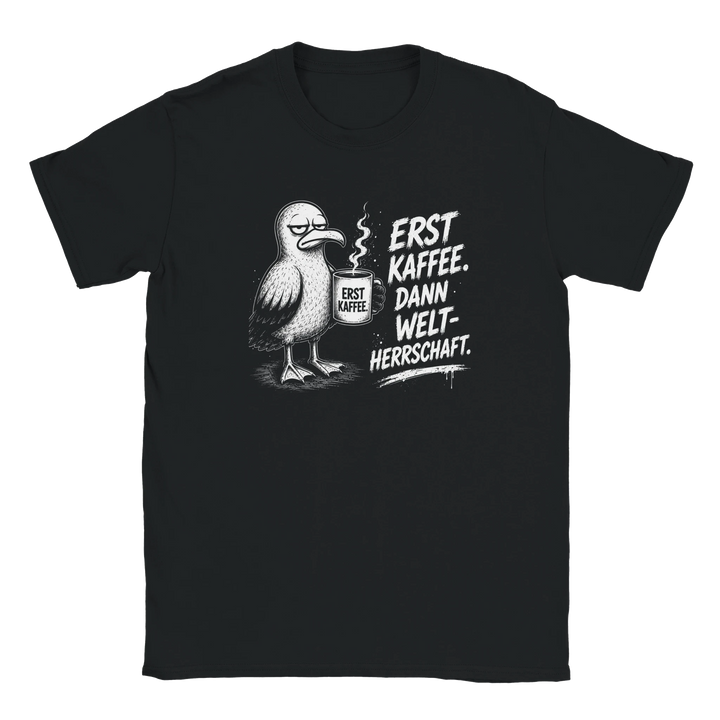 Flatlay des schwarzen T-Shirts mit Möwen-Motiv und Spruch „Erst Kaffee. Dann Weltherrschaft.“ auf grauem Hintergrund