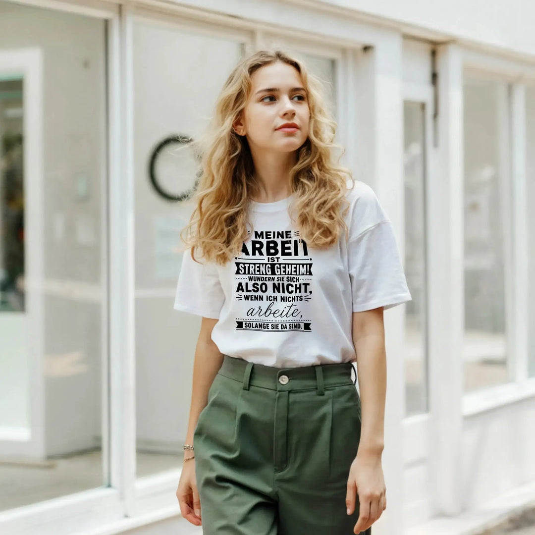 Junge Frau in grüner Hose trägt weißes „Streng geheim“ T-Shirt vor Schaufenster