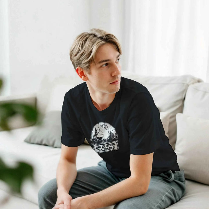 Blonder Mann sitzt entspannt auf einer Couch und trägt das schwarze T-Shirt mit Möwe und Skyline-Motiv.