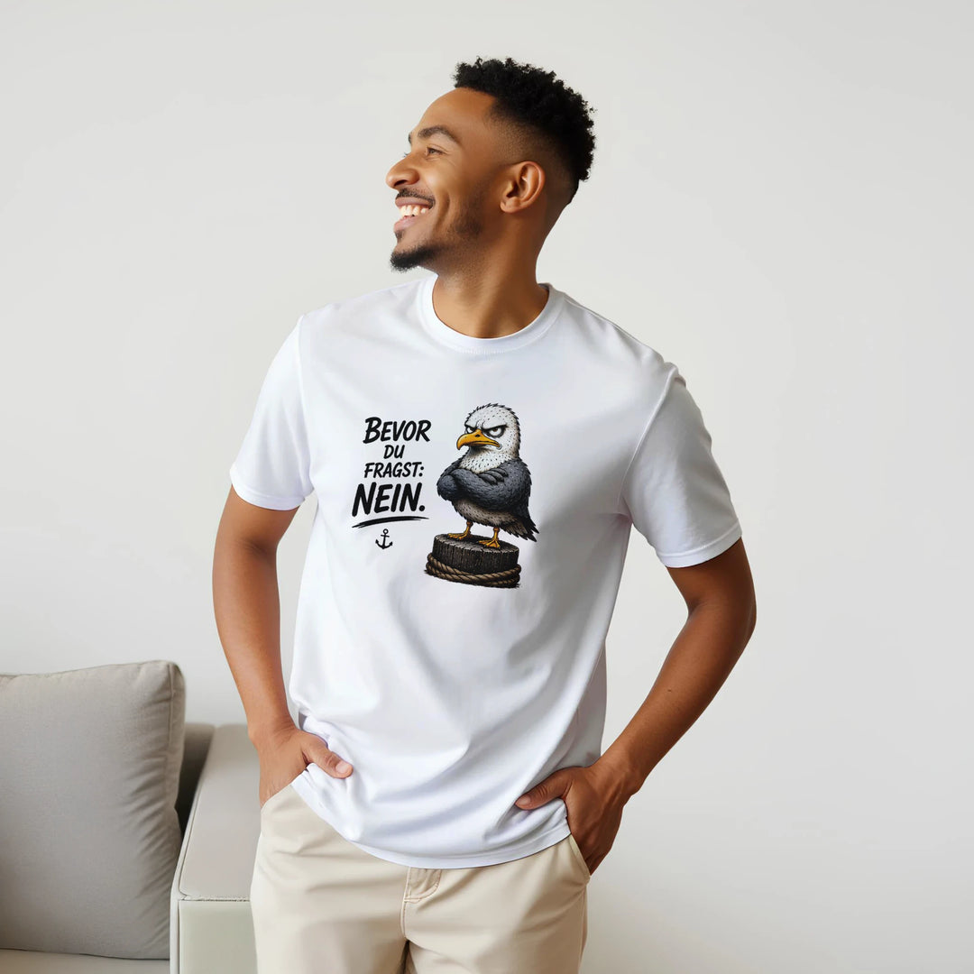 Lachender Mann im weißen T-Shirt steht neben grauem Sofa im Wohnzimmer