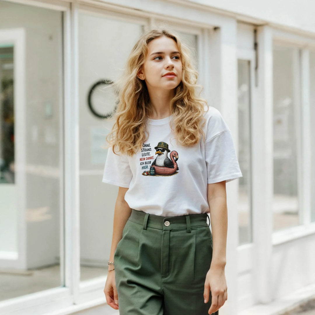 Blonde Frau in grüner Stoffhose trägt das weiße T-Shirt mit Möwen-Print vor einem Schaufenster.