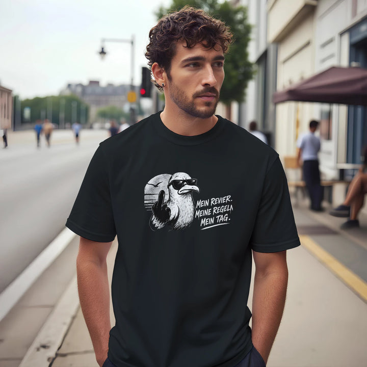 Mann mit lockigem Haar trägt schwarzes T-Shirt mit Möwen-Motiv auf einem Fußgängerweg in der Stadt