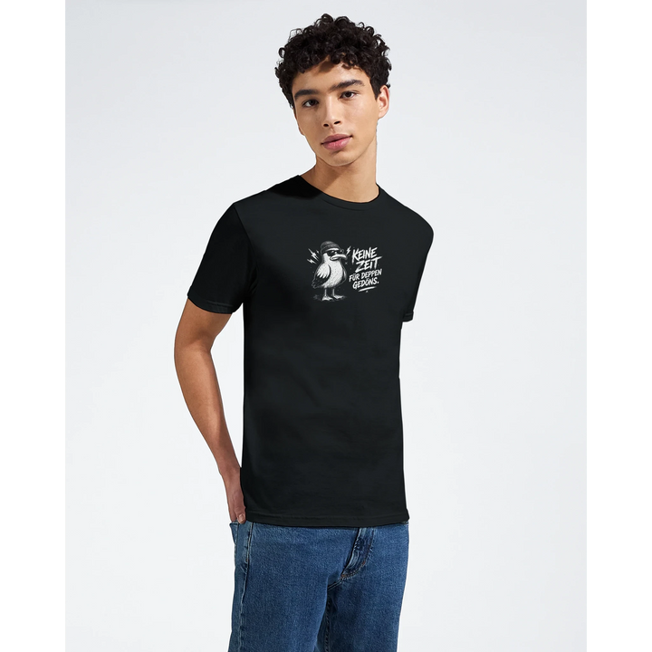 Junger Mann im Halbprofil trägt schwarzes T-Shirt mit Möwen-Print „Keine Zeit für Deppen-Gedöns.“ vor grauem Studiohintergrund.