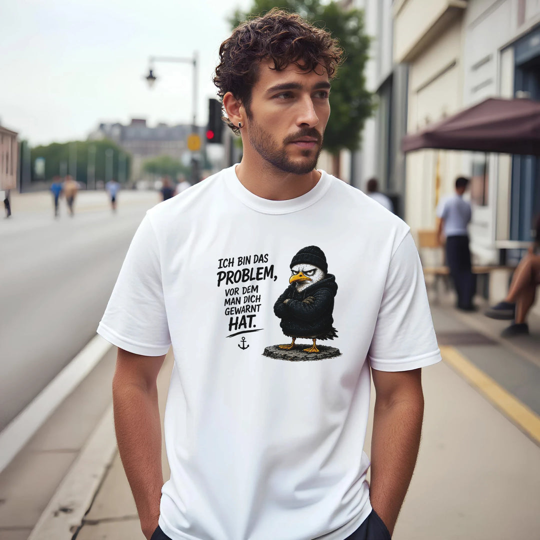 Mann trägt weißes T-Shirt mit Vogel-Print und Spruch 'Ich bin das Problem' auf Gehsteig