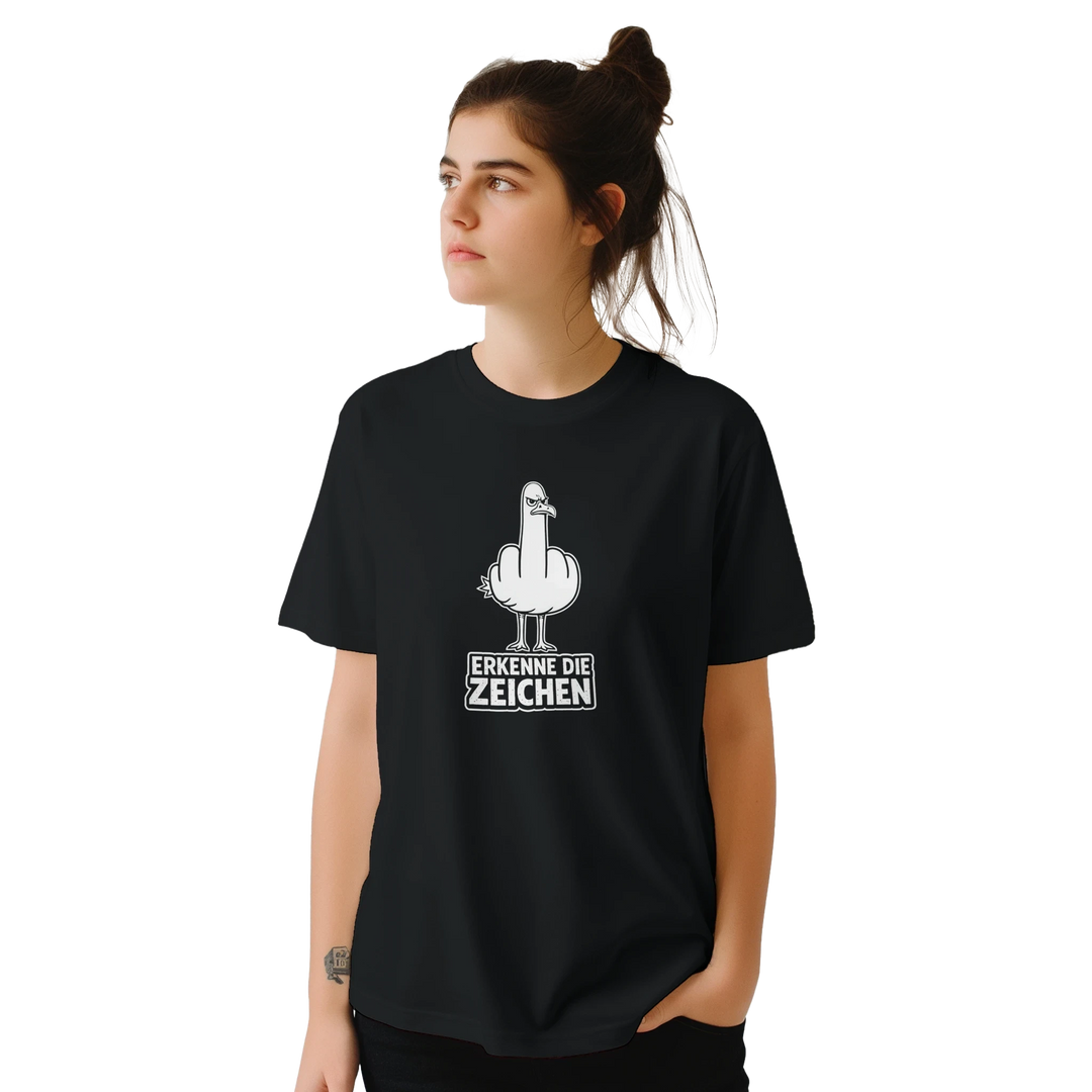 Frau mit Dutt und Armtattoo trägt das schwarze T-Shirt mit Möwen-Stinkefinger-Motiv, Studioaufnahme von vorne.