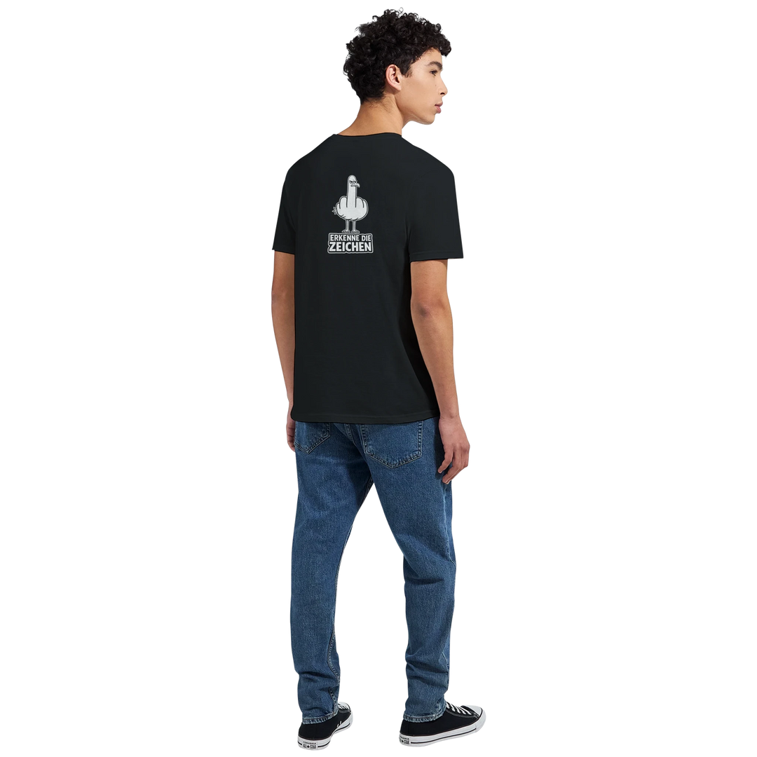 Rückansicht eines Mannes beim Gehen auf der Straße, Möwen-Print und Spruch „Erkenne die Zeichen“ auf dem Rücken des schwarzen T-Shirts.
