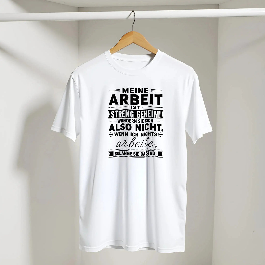 Weißes „Streng geheim“ T-Shirt hängt am Kleiderbügel vor grauer Wand