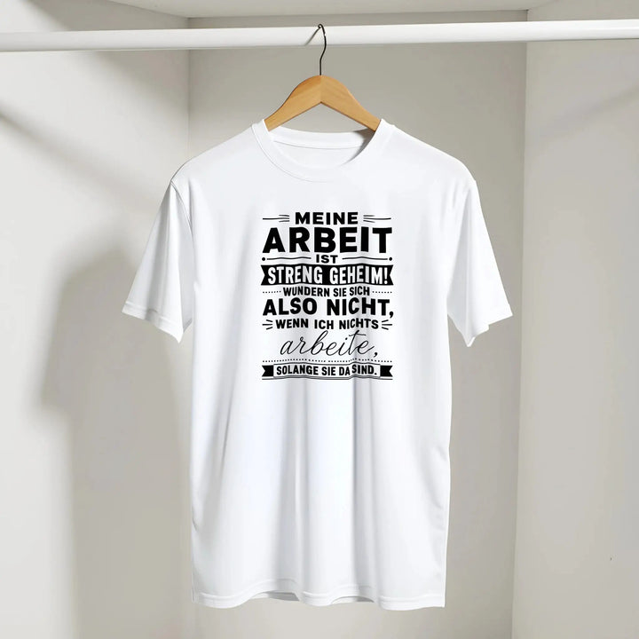 Weißes „Streng geheim“ T-Shirt hängt am Kleiderbügel vor grauer Wand
