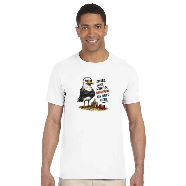 Lächelnder Mann im Studio von vorne, weißes T-Shirt mit grimmiger Möwe neben umgekippter Sandburg und Eimer.
