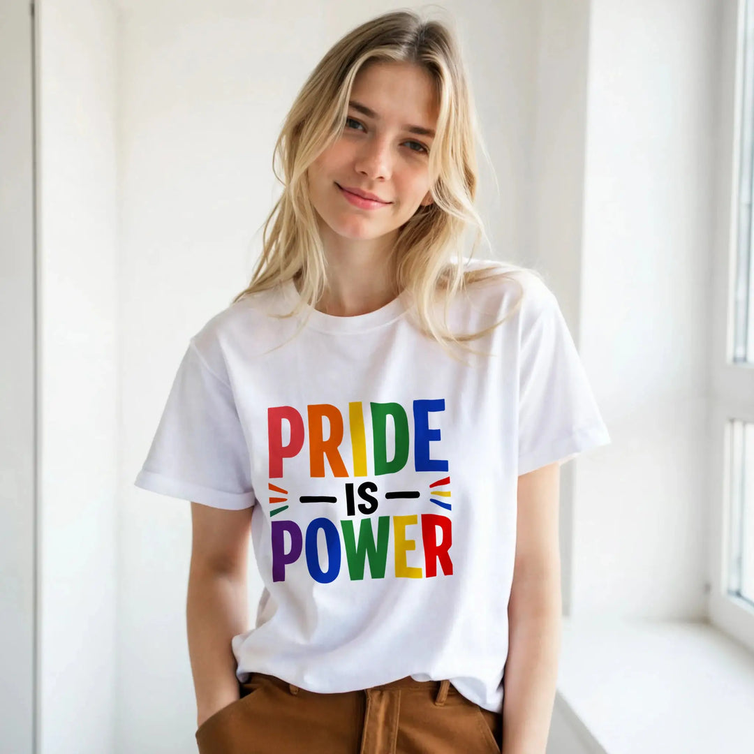 Frau in weißem T-Shirt mit buntem Regenbogen-Schriftzug 'Pride is Power' in hellem Zimmer, Frontalansicht