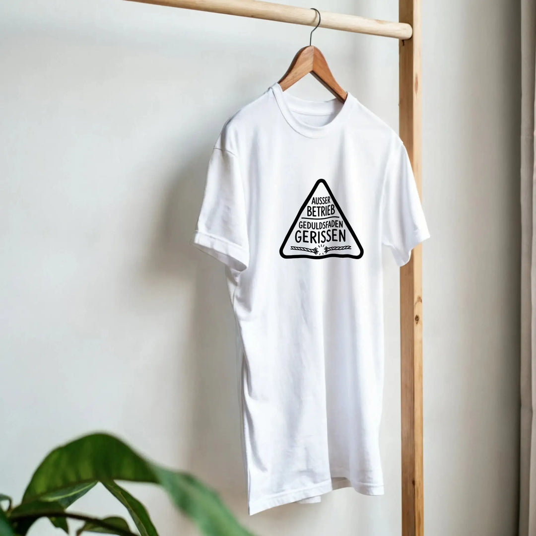 Weißes „Geduldsfaden gerissen“ T-Shirt hängt am Kleiderbügel neben Pflanze