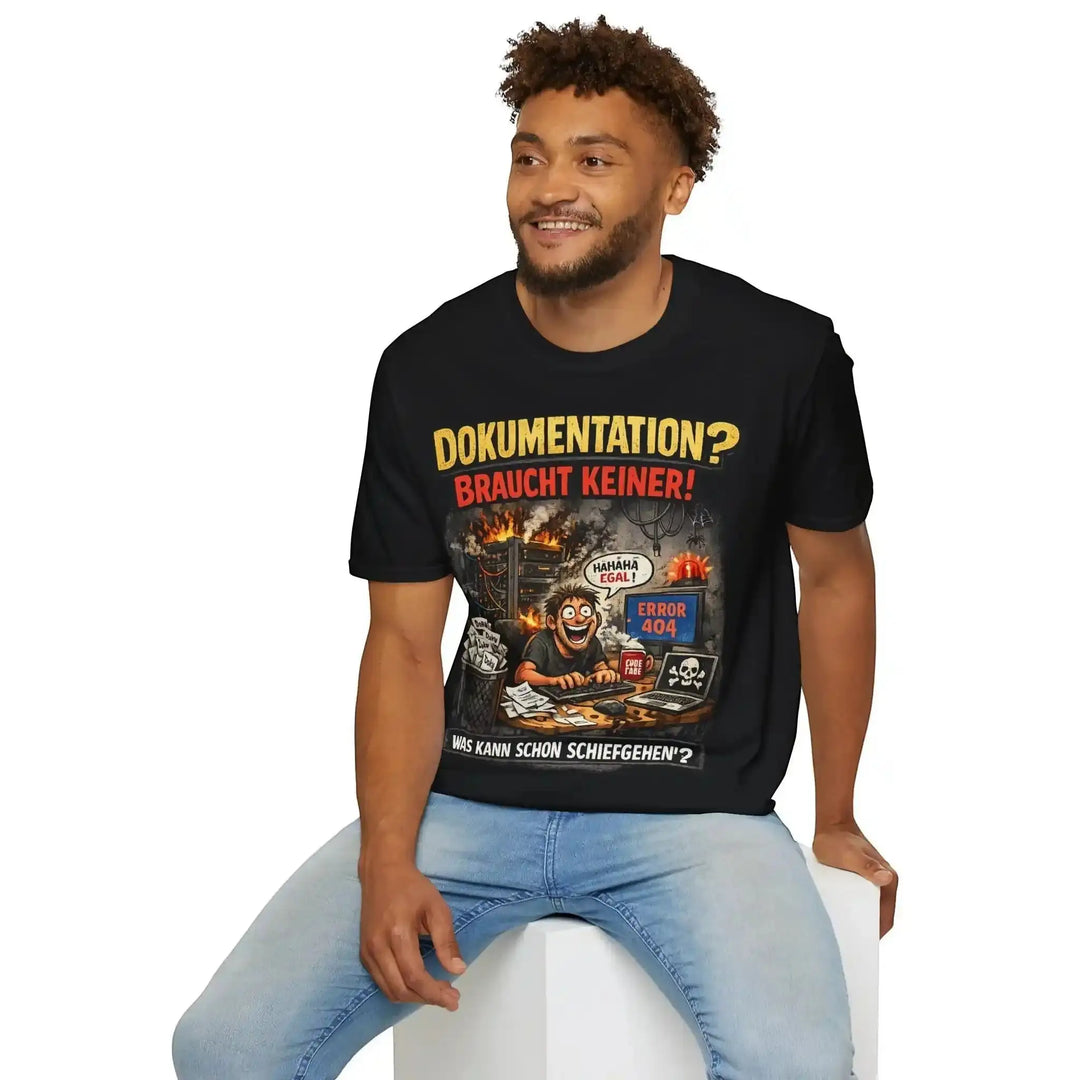 Schwarzes T-Shirt mit Admin-Comic-Print, Mann sitzt lächelnd auf einem weißen Würfel