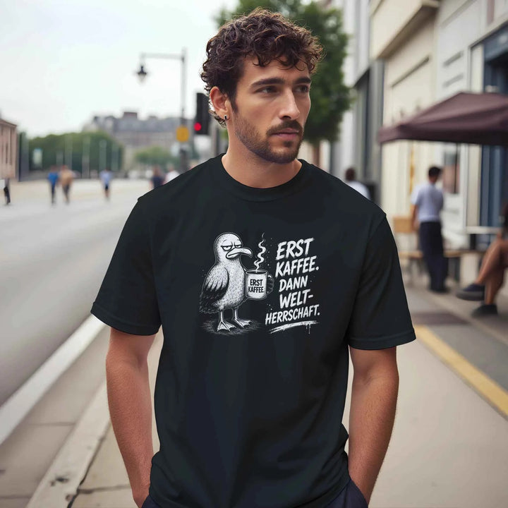 Mann trägt schwarzes T-Shirt mit Möwe und Spruch „Erst Kaffee. Dann Weltherrschaft.“ auf einer Stadtstraße