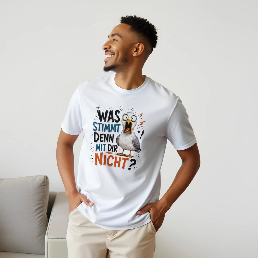 Lächelnder bärtiger Mann trägt weißes T-Shirt mit Möwen-Print im Wohnzimmer, Hände in den Hosentaschen