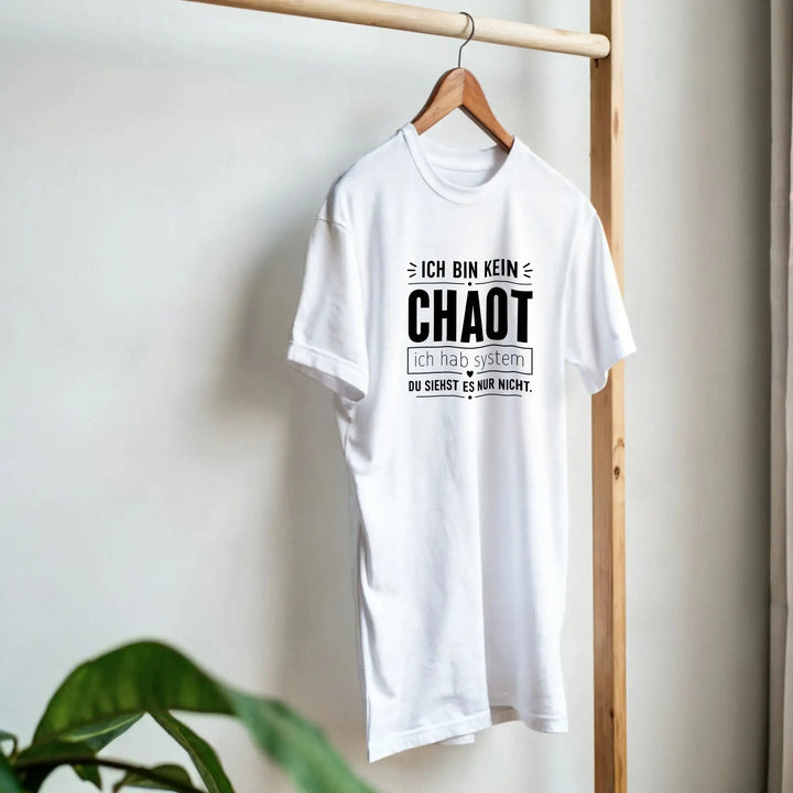 Weißes „Ich bin kein Chaot“ T-Shirt hängt am Kleiderbügel neben Pflanze