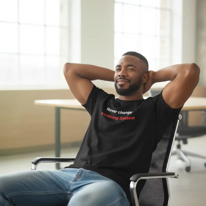 Mann lehnt entspannt in einem Bürostuhl mit den Händen hinter dem Kopf, trägt schwarzes T-Shirt mit dem Aufdruck „Never change a running System“ in modernem Büro.