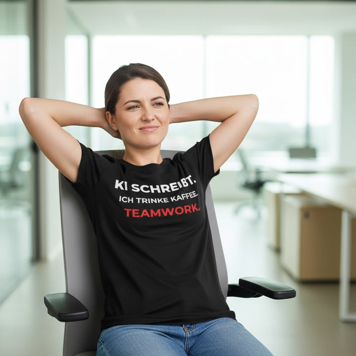 KlareAnsage schwarzes Statement-Shirt mit weißem Text KI schreibt ich trinke Kaffee Teamwork an einer Frau im Büro