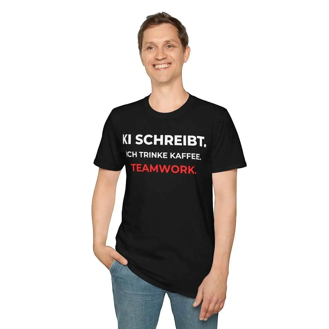 Mann steht vor weißem Hintergrund und trägt schwarzes T-Shirt mit Aufdruck „KI schreibt. Ich trinke Kaffee. Teamwork.“