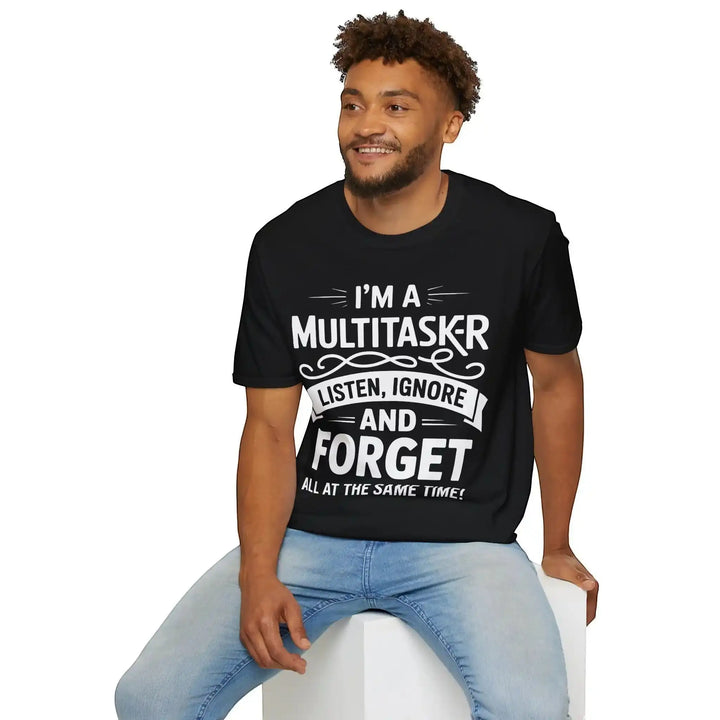 Lächelnder Mann sitzt auf einem weißen Würfel und blickt zur Seite, trägt das schwarze Multitasker-Shirt, Studiofoto.