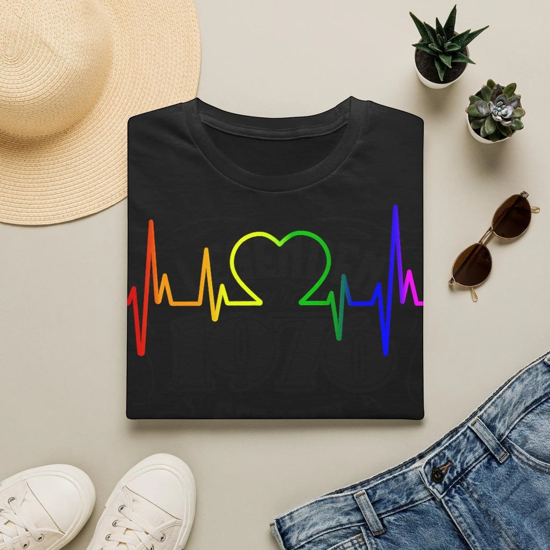 KlareAnsage schwarzes T-Shirt mit Regenbogen EKG-Herzschlag-Print, flach gelegt mit Sonnenbrille und Strohhut